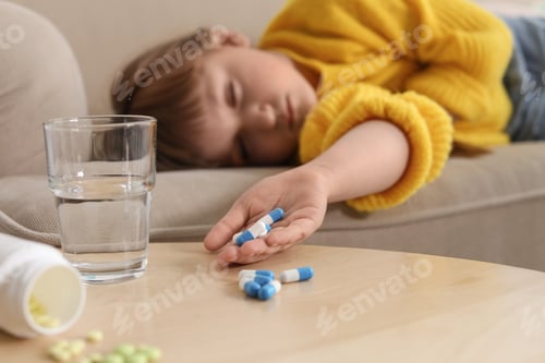 Preview: Unconscious little child with pills on sofa at home. Danger of medicament intoxication