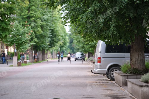 Preview: Passenger van car parked on a city alley street side with blurred walking pedestrians