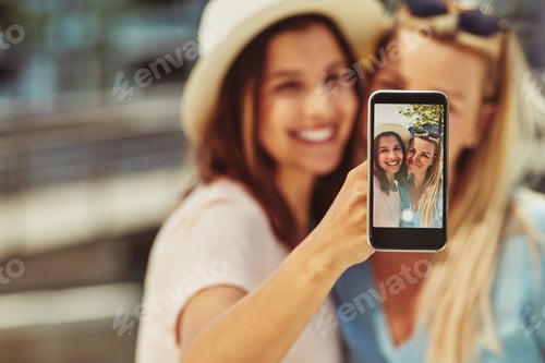 Preview: Two young female friends taking selfies together outside in summer