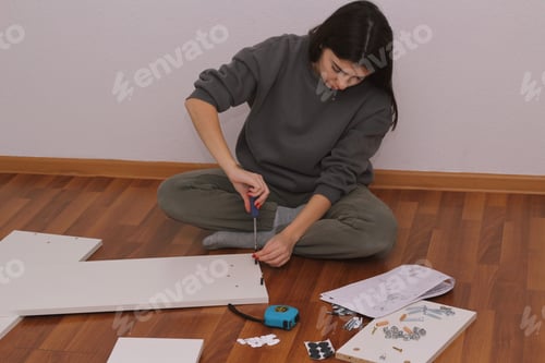 Preview: Young woman collects furniture at home