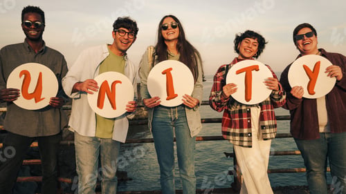 Preview: Diverse group of friends holding letters forming the word UNITY outdoors
