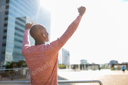 Preview: behind young black man with arms raised and listening to music with earphones