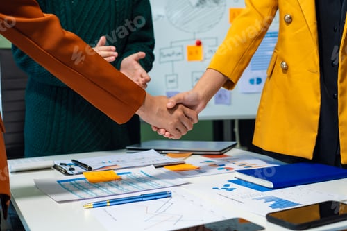 Preview: Happy businessman and businesswoman shaking hands at group board meeting.