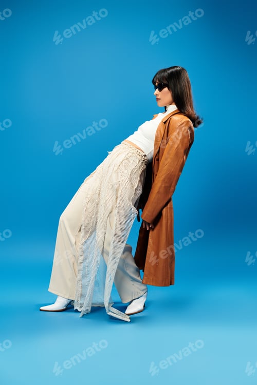 Preview: Stylish young woman showcases modern fashion with flair against a vibrant blue backdrop