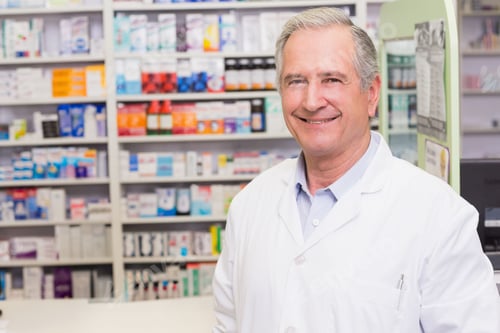 Preview: Senior male pharmacist standing behind pharmacy counter by medicine shelves, info board, copy space