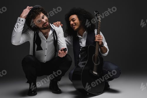 Vista previa: dúo de músicos felices con guitarra y armónica sentados en cuclillas