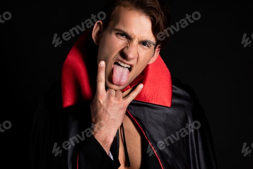 Preview: man in vampire halloween costume sticking out tongue and showing rock sign isolated on black