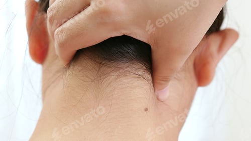 Preview: Back view of Asian woman using hands to massage the nape of her neck in physical therapy to reduce p