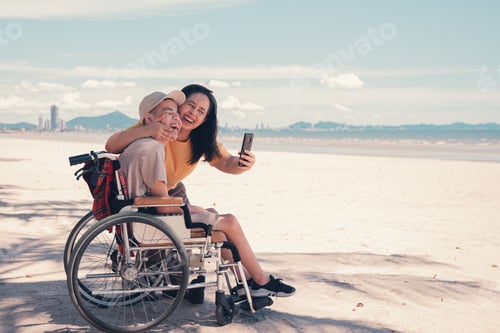 Preview: Happy mother and disabled teenage boy on wheelchair use social media, Sea beach background.