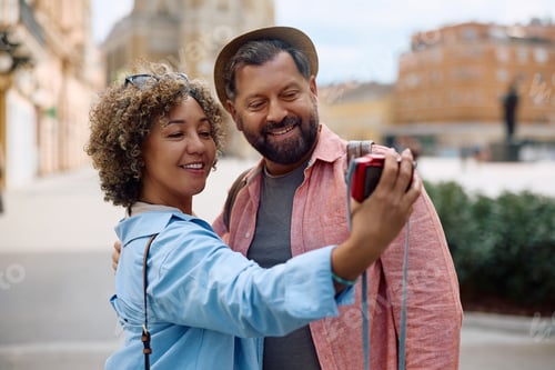 Preview: Happy tourist couple taking selfie with photo camera while sightseeing during their trip.