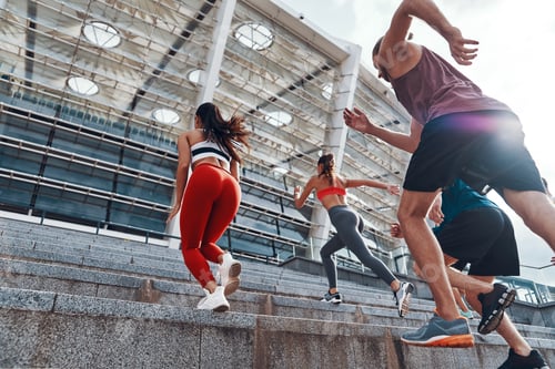 Preview: Group of young people in sports clothing jogging while exercising on the stairs outdoors