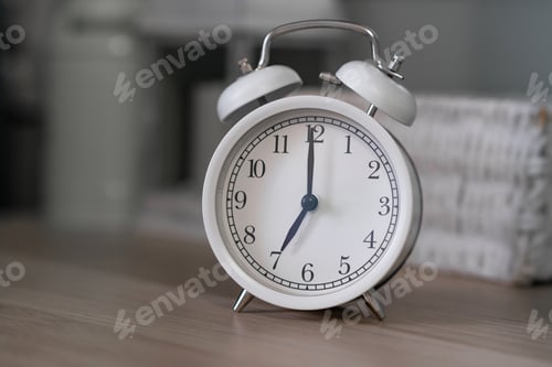 Preview: Close-up of a round white alarm clock on a table in the bedroom.