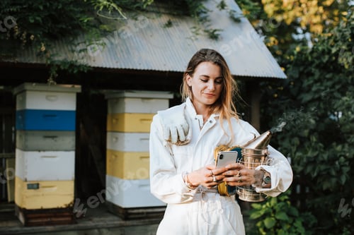 Preview: Woman Beekeeper Holding Phone Near Beehives Outdoors
