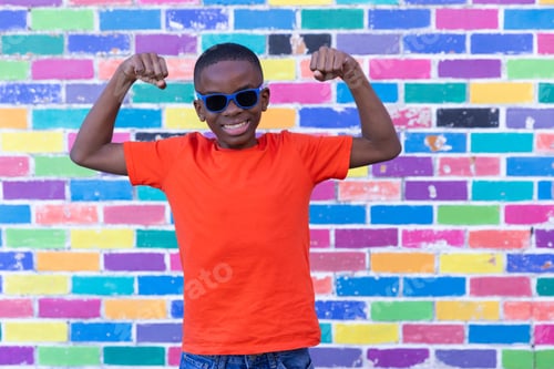 Preview: Smiling boy in sunglasses flexing muscles in front of colorful brick wall