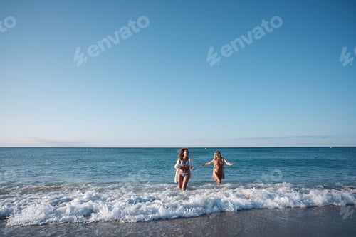 Preview: Two women running into the ocean on a sunny day