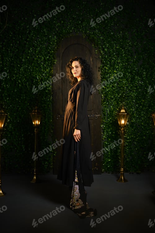 Preview: Woman stands in front of doorway with greenery and lamps in indoor setting at night