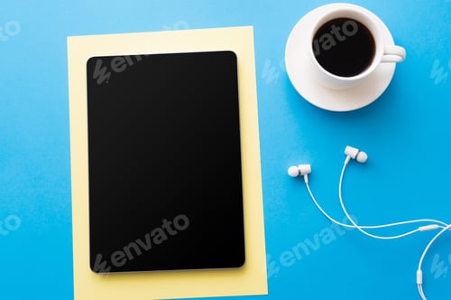 Preview: top view of digital tablet with blank screen near cup of coffee and wired earphones on blue