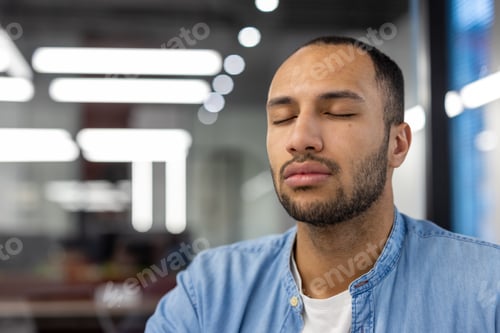 Preview: Close-up photo of young hispanic man sitting at workplace in office with closed eyes and resting