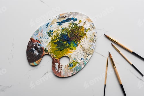 Preview: top view of colorful palette with oil paints near paintbrushes on marble white surface