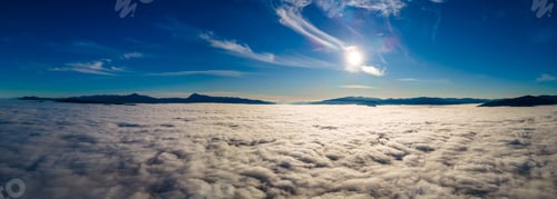 Preview: Aerial view of yellow sunset over white puffy clouds with distant mountains on horizon