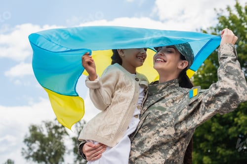 Preview: smiling woman in camouflage holding ukrainian flag with daughter outdoors