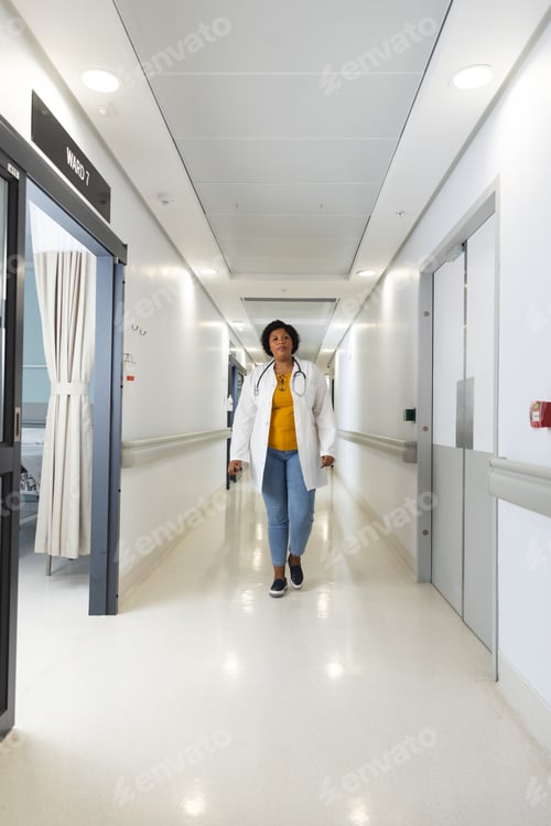 Preview: African american female doctor wearing lab coat and stethoscope walking in corridor at hospital