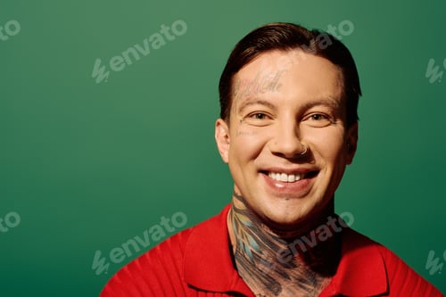 Preview: A young man with tattoos smiles brightly against a vibrant green background in a playful portrait