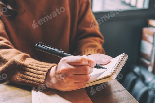 Preview: Closeup image of a woman holding and writing on blank notebook with fountain pen on wooden table