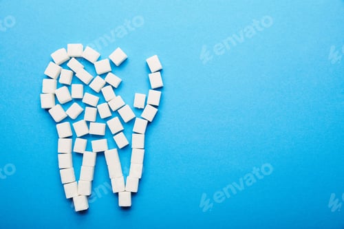 Preview: top view of white sugar cubes arranged in tooth sign on blue background, dental care concept