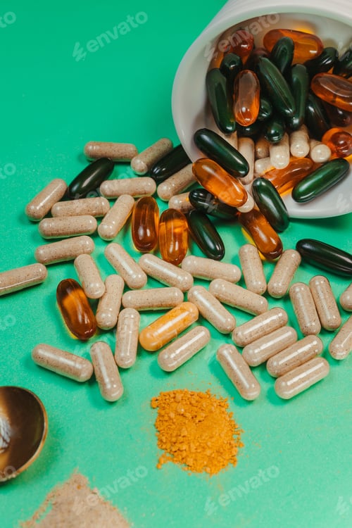 Preview: Green tabletop with an array of vitamin supplement capsules and pills and a spoon