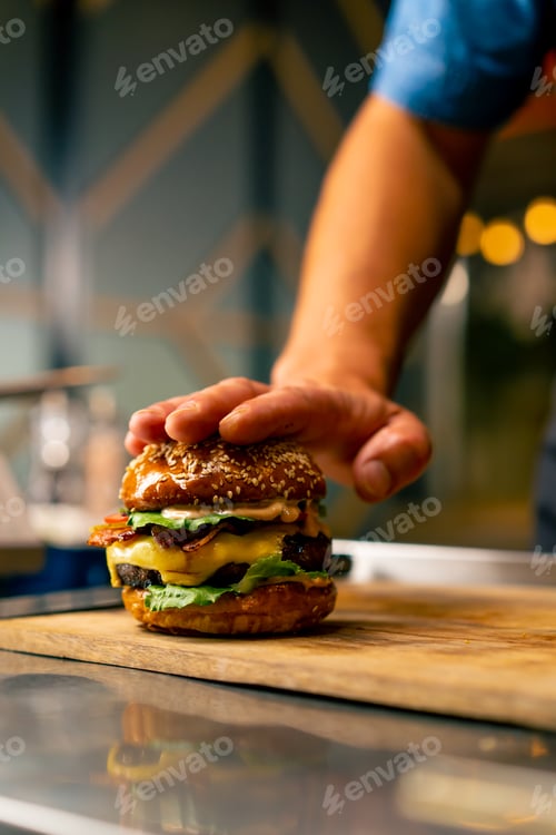 Preview: Close-up of a chef pinning a burger with beef patty with vegetables and cheese cooked in the kitchen