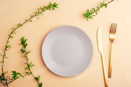 Preview: Gray plate and cutlery on light peach background with cherry blossom branches. Top view, flat lay