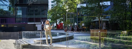 Preview: Stylish corporate woman in suit, standing with laptop and work documents, using mobile phone