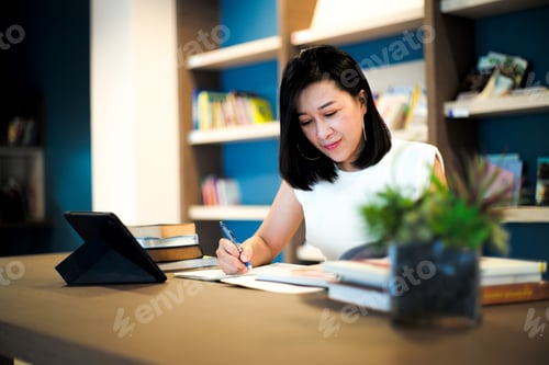 Preview: Portrait beautiful Asian woman works at the home office with blurred shelf of books in background