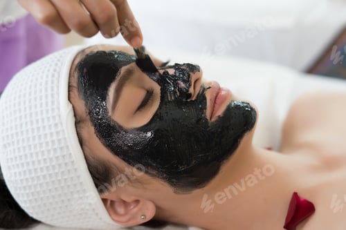 Preview: Beautiful woman getting facial black mud mask at beauty salon.