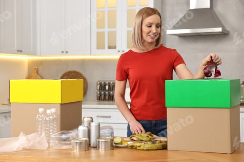 Preview: Smiling woman separating garbage at table in kitchen