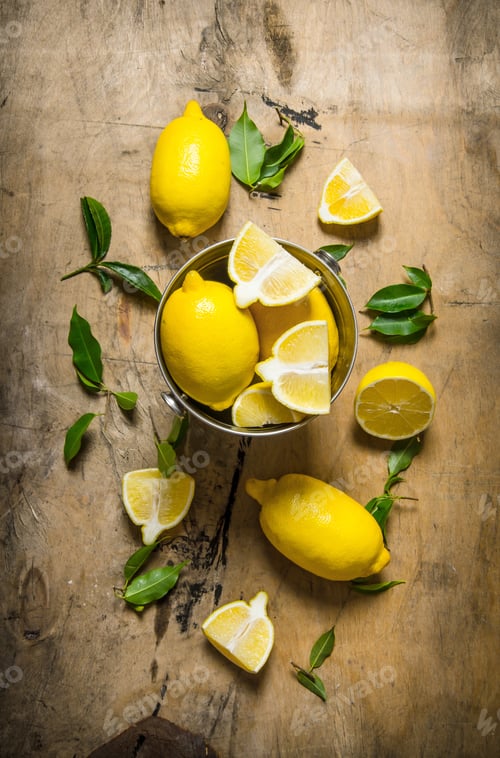 Preview: Fresh lemons in a bucket of leaves. On wooden table.