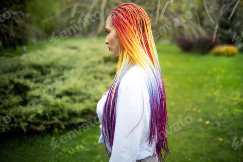 Preview: Confident girl with colored makeup and colored braids in fashionable clothes posing against the