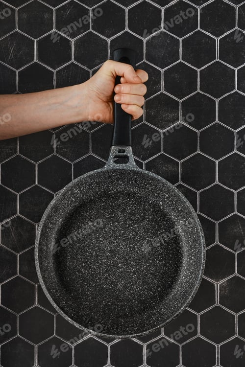 Preview: A hand holding a non-stick frying pan against a hexagonal patterned dark wall