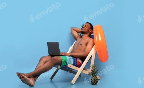 Preview: Relaxed black guy chilling in lounge chair with laptop computer, working online from tropical