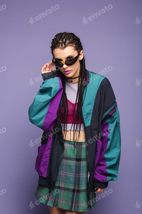 Preview: Young woman in retro sports jacket holding sunglasses on purple background