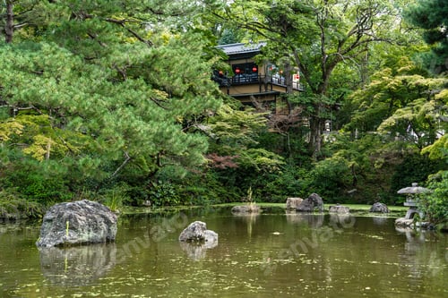 Preview: Japanese tea house nestled in lush greenery overlooks a pond with stones and a weathered lantern.
