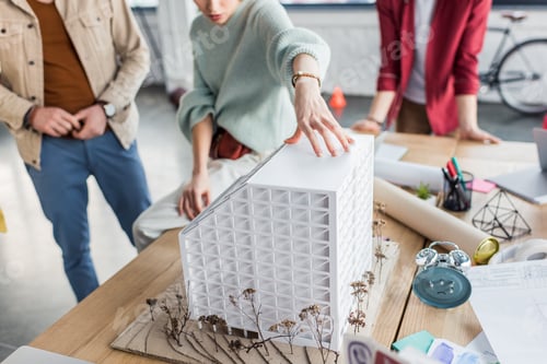 Preview: cropped view of group of female and male architects working together on house model in loft office