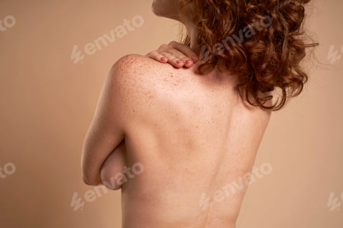 Preview: Back view of unrecognizable naked red head woman covering her breast with hands