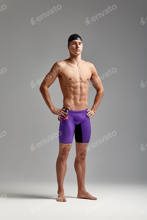 Preview: Young attractive swimmer in excellent physical shape in purple swimming shorts, on a gray background