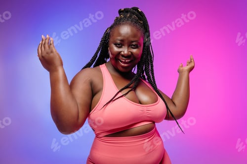 Preview: Beautiful African curvy woman in sportswear gesturing and smiling against vibrant background