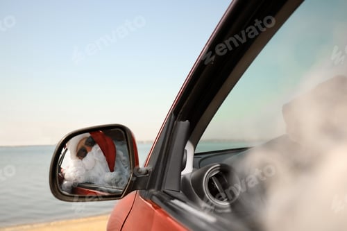 Preview: Authentic Santa Claus looking into side view mirror of car near sea