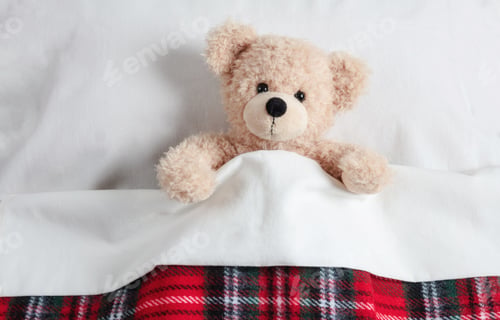 Preview: Cute teddy covered with a warm blanket, laying in bed