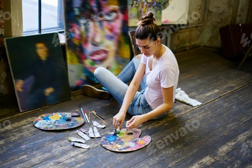 Preview: Young Caucasian woman with pallet choosing oil or acrylic colors during art workshop in loft studio