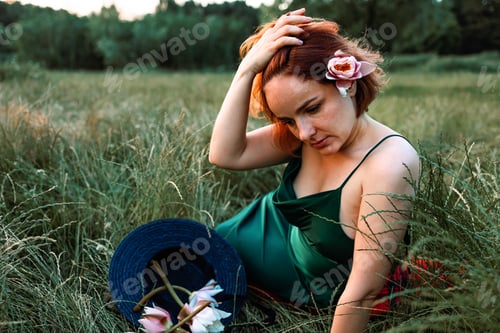 Preview: Summer lifestyle portrait of beautiful young woman holding water lily flowers. sitting in the field